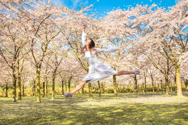Šťastný dospívající, on se směje a vyskočil v kvetoucí třešňov — Stock fotografie