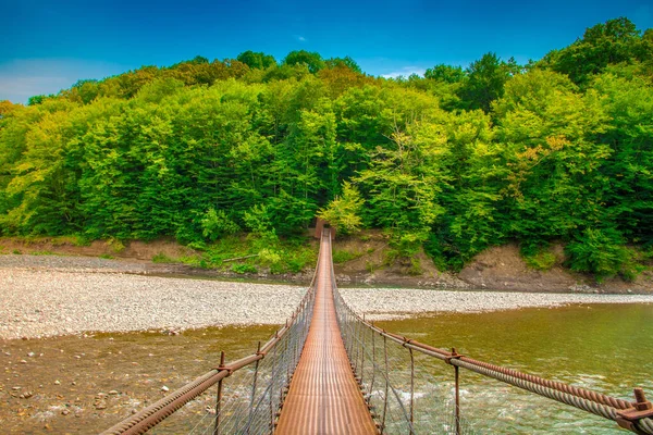 Iron suspension bridge. A suspension bridge leads over a mountain river
