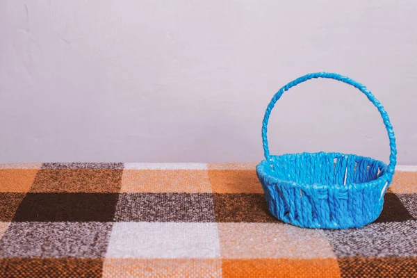 A blue empty basket sits on the table on a checkered tablecloth