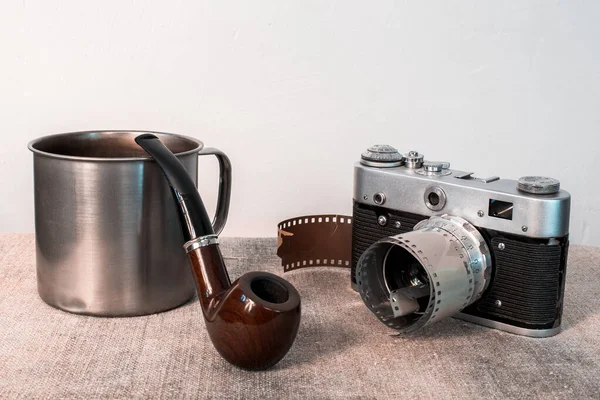 Still life, camera, Smoking pipe and iron mug on . Gray background.