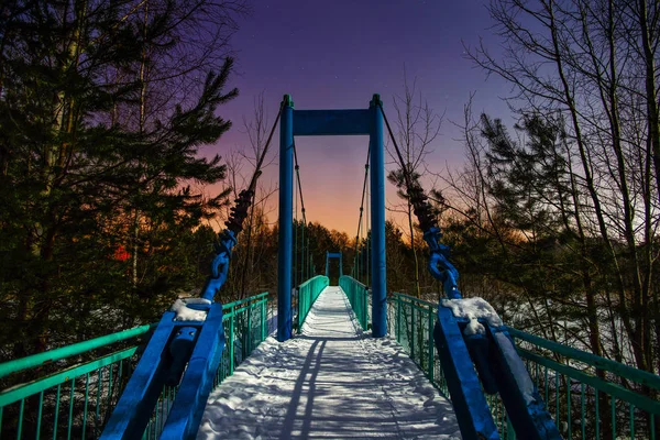 Snow-covered suspension bridge illuminated by moonlight