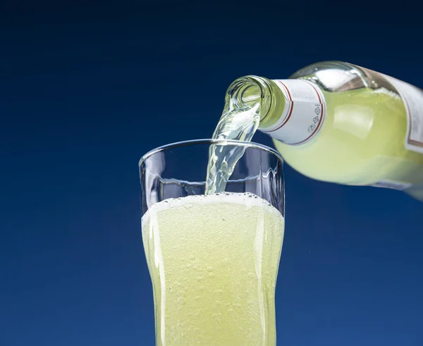 Carbonated drink pours from a glass bottle into a glass