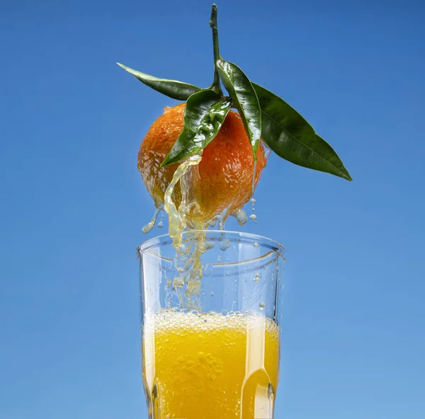 Orange juice flowing down the leaves and surface of an orange into a glass