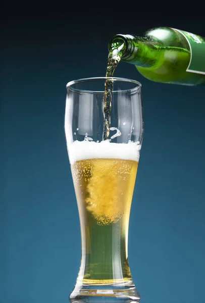 Beer is pouring from the neck of a bottle into a beer glass