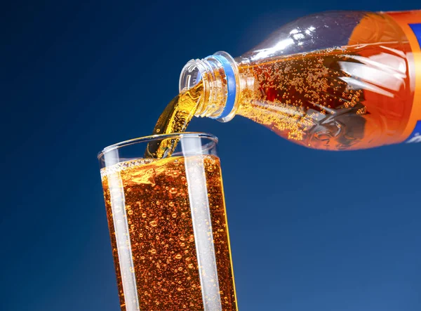 Yellow-orange carbonated drink is pouring from a bottle into a glass