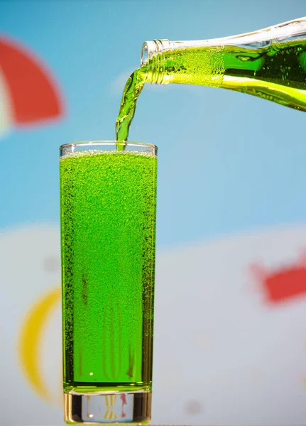 Tarragon carbonated drink is pouring from a bottle into a glass