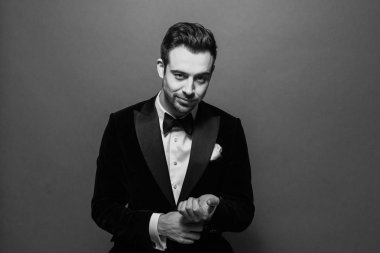 Siyah beyaz portre işadamı bir takım elbise, beyaz gömlek ve kravat, kol düğmesi koyarak ve düz studio arka plan karşı kamera bakıyor.