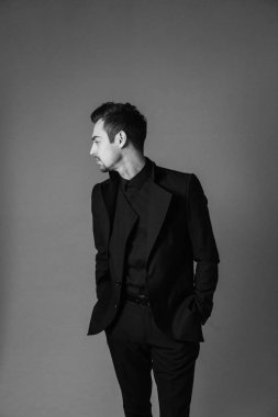 Ayakta, elleri ceplerinde ve düz studio arka plan karşı tarafa bakarak genç yakışıklı bir adam bir takım, siyah beyaz portre.