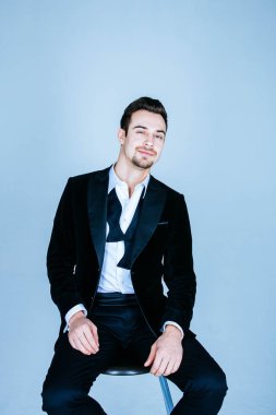 Bir takım, oturma ve kamera, papyon, geri düz studio arka planı arıyorum genç yakışıklı bir adam portresi