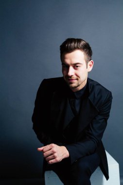 Oturma ve kamera düz studio arka plan bakarak bir takım, yakışıklı bir genç adam portresi.