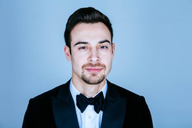 Kameraya düz studio arka plan karşı ciddi görünümlü genç yakışıklı bir adam bir takım, portresi.