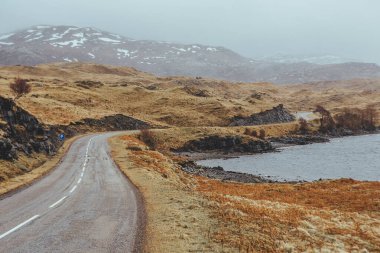 İskoçya dağlarında bir vadide göl boyunca uzanan bir yolun manzarası