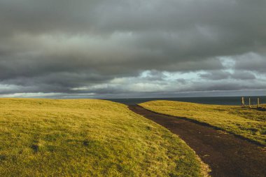 İskoçya 'nın kuzey kıyılarındaki Brora köyü yakınlarındaki yeşil tarlalar ve kıyı yolu üzerinde güneş ışığı.