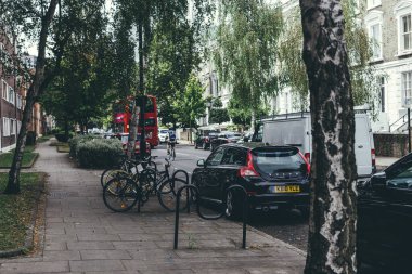 Londra / İngiltere-30 / 7 / 18: kaldırımda kimsenin olmadığı bir Londra banliyö sokağının yaşam tarzı fotoğrafı, park edilmiş arabalar ve bisikletlerin yanı sıra kırmızı bir çift katlı otobüs, bisikletçi ve yoldan geçen bir minibüs