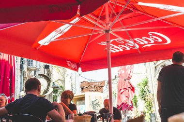 Tel Aviv / İsrail-10 / 10 / 18: Sıcak bir yaz gününde kırmızı paraşüt örtüsünün altındaki bir sokak kafesinde insanlar gevezelik ediyorlar.