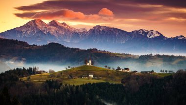 Gündoğumunda St. Thomas Kilisesi. Arka planda Kamnisko Savinjske Alpe, Slovenya Skofja Loka.