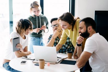 Toplantı iş arkadaşlarınızla Beyin fırtınası sürecinde. Grup hipsters düşünme parlak modern ofisindeki yeni projede ve arkadaş farklı elektronik aygıtlar kullanarak.