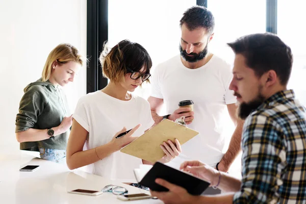 Group of hipsters is discussing new start up project and communicating with friends by using mobile phones. International student group is arranging a seminar on a digital marketing theme.