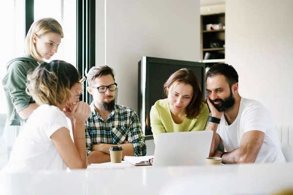 A group of web designers and quality engineers is testing the new web site on the laptop during the scrum meeting. Young hipsters are working on a new start up project in a modern coworking space.