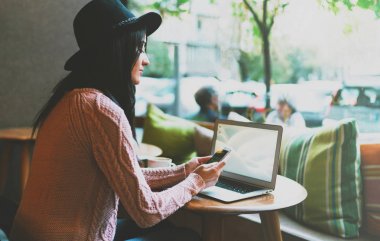 Taşınabilir bir bilgisayar ve bir tablet Web'de bilgi arama yeni bir projede çalışan genç profesyonel serbest meslek. Beyaz boş sınıf başkanı ile belgili tanımlık laptop oturan şapkalı güzel kız