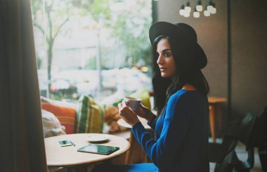 Serbest meslek sahibi kadın kahve molası sırasında e-postaları bir tablet bilgisayarda okuma. Şapka uzun siyah saçlı güzel öğrenci kız elektronik cihazlar modern bir kafede oturuyor.