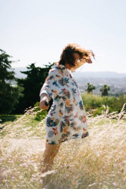 Genç beyaz kadın alanının yürürken rüzgarlı ve sıcak güneşli gün keyif alıyor. Renkli elbise giyen çekici kadın rahatlatıcı bir yaz gününde açık havada. Defocusing içinde kız