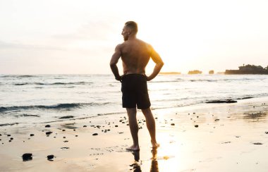 Vahşi kum plaj deniz bakarak bir sportif adam silüeti. Eril erkek çıplak gövde ile mal denizde bitmiş akşam eğitiyor. Yaz egzersiz eğitim açık havada.