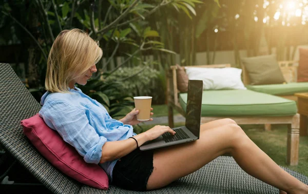 年轻成功的自由职业者女性享受早晨咖啡 而工作在便携式计算机在暑假期间 在游泳池边放松的时候 金发女郎在笔记本电脑的显示屏上阅读电子邮件 — 图库照片