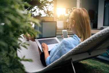 Çekici öğrenci kız havuz başında tatil sırasında rahatlatıcı ve cep telefonu ve dizüstü bilgisayar tarafından arkadaşlarınızla sohbet. Genç kadın bir smartphone ve boş ekranlarla taşınabilir bir bilgisayar ile oturuyor.
