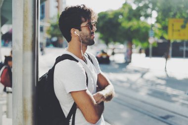 Güneş gözlüğü takıyor siyah kıvırcık saçlı sakallı adam sırt sırt çantası ile bir istasyon tren bekliyor. Yakışıklı genç erkek bir sokakta duran cep telefonuna müzik dinlemek.