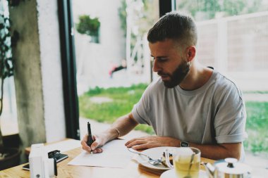 Yaratıcı web Illustrator çizimleri yeni bir proje için bir kafede bitkisel çay rahatlatıcı tadını çıkarırken yapıyor. Yetenekli raslantı giyimli öğrenci diploma projesi için Not Defteri'nde notlar yapma.