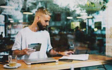 Kablosuz ağa bağlı bir tablet bilgisayar basılı tutarak kağıtları arayan akıllı öğrenci. Başarılı freelancer modern bir kafede otururken yeni bir proje için yeni fikirler yazma.