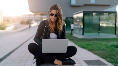 Güzel beyaz kadın şehir alanı wi-fi için bağlı bir dizüstü bilgisayar ile oturuyor. Genç girişimci açık havada bir bulanık kentsel arka plan üzerinde otururken bir taşınabilir bilgisayarda çalışıyor.
