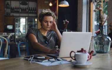 Hippi kız e-postaları modern bir taşınabilir bilgisayar ekranında bir kafede otururken okuyor. Genç iş kadını modern bir kafede kahvaltı ederken skype çağrısı için bekliyor.