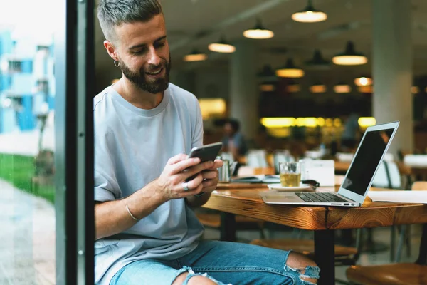 Leende Skäggig Ung Man Textning Meddelanden Mobiltelefon Medan Chattar Med — Stockfoto