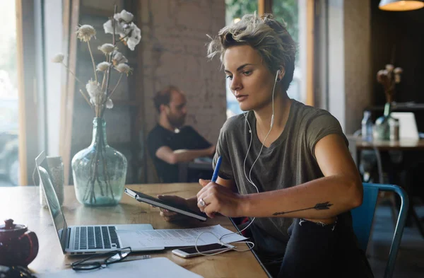 モデル顔の若い女性は コーヒー ショップに座っているポータブル コンピューターを使用して 週末旅を予定です 女性フリーランサーがモダンなカフェで働いている間ノート パソコンを使用してください — ストック写真