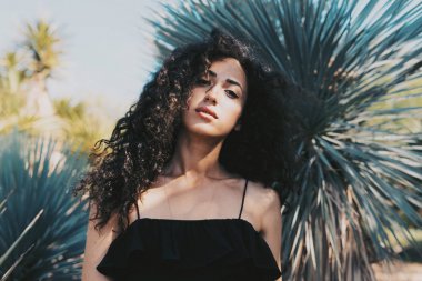 Esmer kız açık havada Şehir Parkı, çiçekler ve çalılar arka plan ayakta iken kameraya bakıyor. Siyah yazlık elbise giyen modeli göz kadın Garden'da günbatımı üzerinde yürüyor.