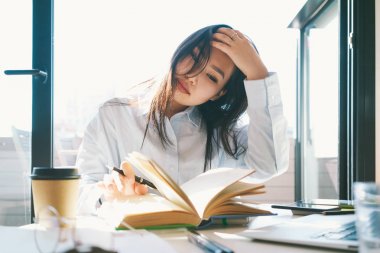 Üniversite öğrencisi güneşli bir büyük pencere yanında otururken ders kitabı okuyor. Genç girişimci kadın yeni ürün tanıtımı için hazırlanırken bilgi arama.