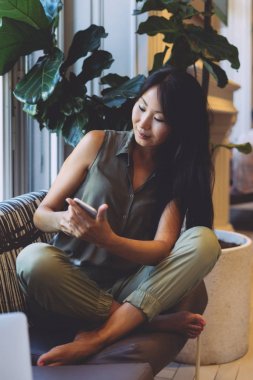 Büyüleyici bir Asya Güzellik blogger ile modern iç bir kafede otururken yanında smartphone mesaj atıyor. Çekici kadın kahve molası sırasında iş e-postalarınızı okuyor.