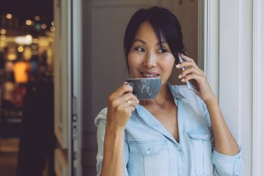 Güzel Asyalı kadın modern bir kafede kahve ile ara yaparken cep telefonuyla konuşuyor. Genç girişimci iş ortakları ile toplantı telefon tarafından atanması.