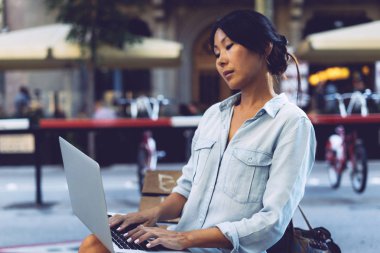 Güzel Asyalı kadın şehir kafede wi-fi için bağlı bir dizüstü bilgisayar ile oturuyor. Genç girişimci açık havada bir bulanık kentsel arka plan üzerinde otururken bir taşınabilir bilgisayarda çalışıyor.