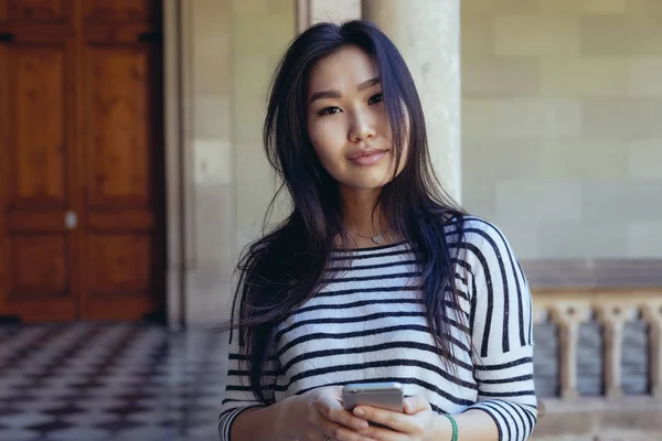 Portrait of the beautiful model look asian woman looking at the camera and holding a mobile phone in hands. Hipster girl wearing casual clothes it texting to the friends by a smartphone.