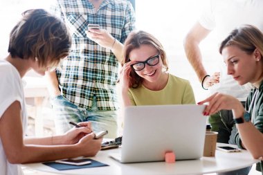 Bir grup web tasarımcıları ve kalite mühendisleri laptop yeni web sitesinde scrum toplantı sırasında test ediyor. Genç hipsters projeyi modern coworking uzayda yeni bir başlangıç üzerinde çalışıyoruz.