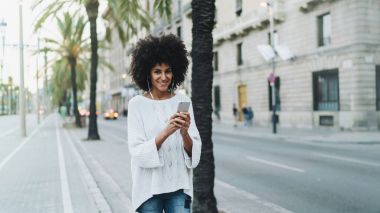 Cep telefonu ile şehir yürürken arkadaşıyla genç hippi kız communicationg. Hippi kız açık havada rahatlatıcı bir müzik ile indirilen ve bir akıllı telefon üzerinde oynanan online programları gülümseyen.