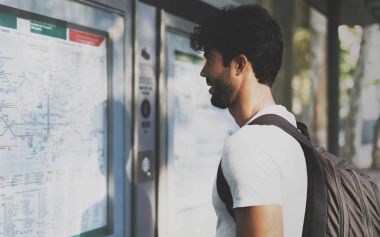 Genç bir toplu taşıma sistemi Haritadaki rota bilinmeyen şehirde arama interantional öğrenci sakallı. Bir tren istasyonu tren Uçus tarifesi bakarak sırt çantası ile yakışıklı Gezgin.