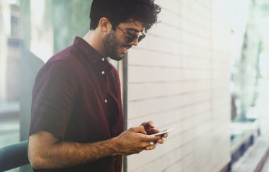 Yakışıklı sakallı serbest meslek sahibi şık güneş gözlüğü takıyor bir smartphone bir ekranda iletileri okur. Genç başarılı iş adamı bir cep telefonuna bir sokakta duran iş e-posta okuma.