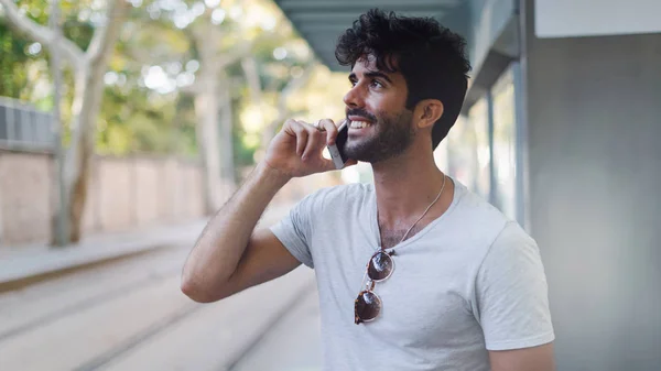 Young blogger is happy to receive good references from the critics by a mobile phone call. Cheerful bearded hipster guy is talking with friends by a smartphone while standing outdoors.