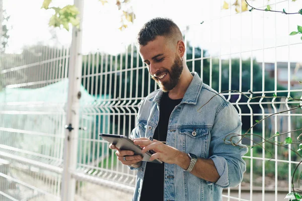 に接続されているタブレットで社会的なネットワーク アプリケーションを使用した屋外の自由な時間を過ごす笑顔の若い留学生ネット ポータブル コンピューターでハンサムなひげを生やした男でサーフィン ウェブ — ストック写真