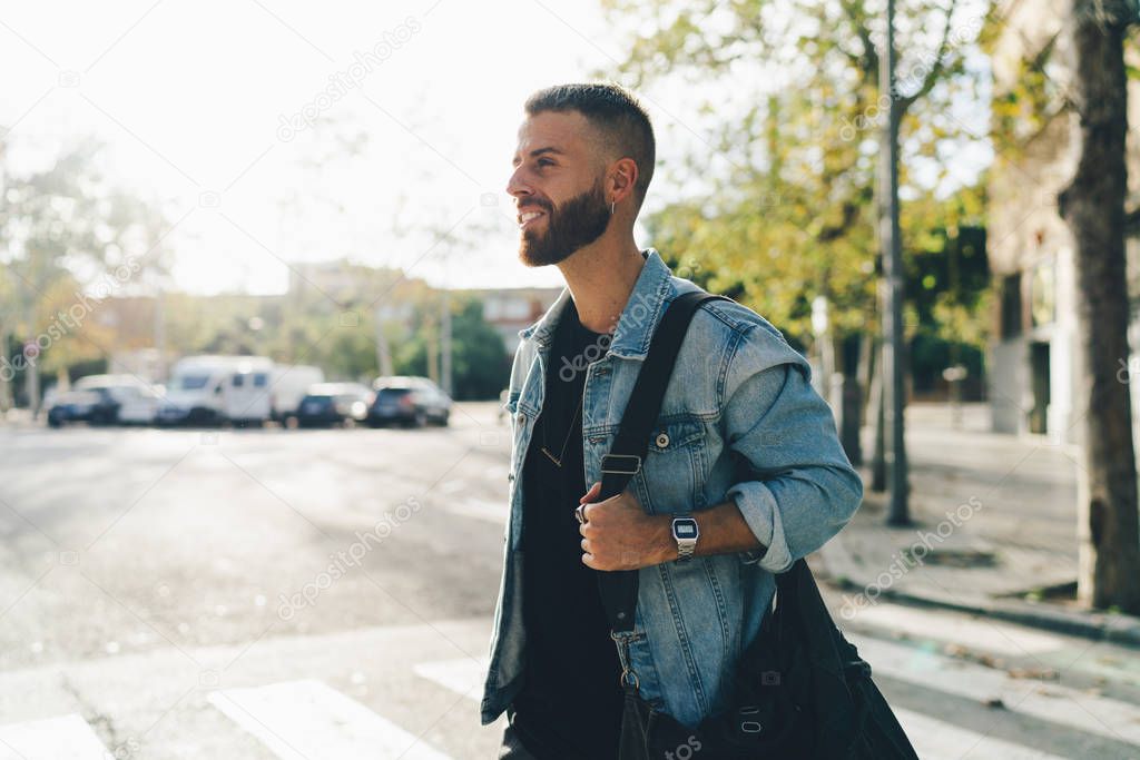 Smiling international student walking the city he came for the study on a late summer day. Bearded hipster guy wearing stylish clothes crossing the road and going to the gym in the sunny morning.