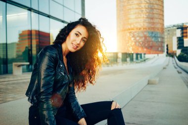 Açık havada poz ve kameraya bakarak uzun kıvırcık saçlı moda kadın portresi